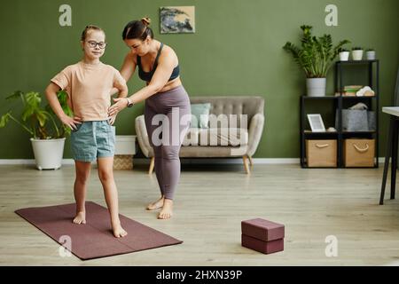 Portrait en longueur de la jeune fille avec le syndrome de Down s'exerçant à l'intérieur avec une femme instructeur assistant, copier l'espace Banque D'Images