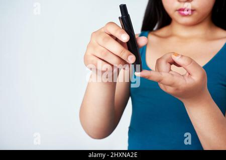 Restez au courant et frappez ce diabète. Photo en studio d'une jeune fille utilisant un test de glycémie sur son doigt contre un fond gris. Banque D'Images