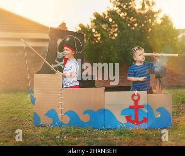 Qui a besoin de jouets quand vous avez de l'imagination. Photo d'un petit garçon mignon et de son frère jouant des pirates dehors sur un bateau fait de boîtes en carton. Banque D'Images