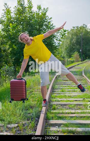 un voyageur riant avec une valise rouge marche le long des rails Banque D'Images