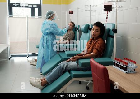 Jeune femme hispanique qui donne son sang aux patients malades de l'hôpital tout en étant assise dans un fauteuil dans une grande salle Banque D'Images