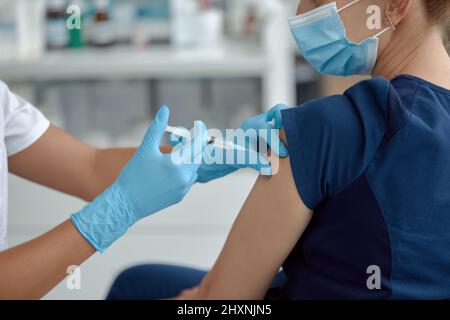 Femme dans le masque médical se faire injecter à l'hôpital. Médecin ou infirmière préparant une seringue pour donner un cliché à une patiente Banque D'Images