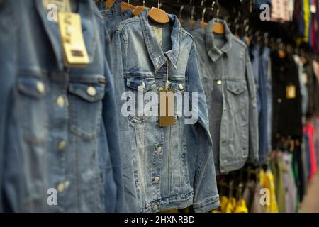 La veste en denim est suspendue sur le cintre en magasin. Détails des ventes de vêtements. Des choses pour les enfants et les adultes dans le centre commercial. Des vêtements pour tous les jours. Banque D'Images