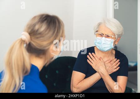 Une femme âgée se sent mal et malade, touchant sa poitrine et se plaignant de douleurs cardiaques à son soignant. Photo de haute qualité Banque D'Images
