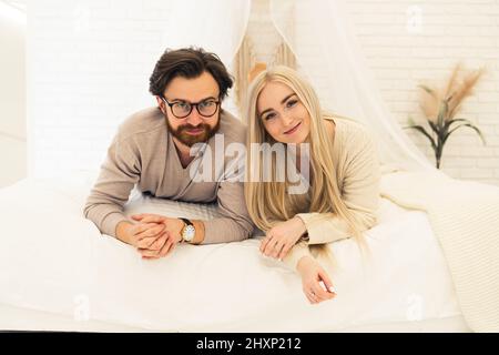 Jeune marié couple caucasien souriant à l'appareil photo couché sur le portrait de lit . Photo de haute qualité Banque D'Images