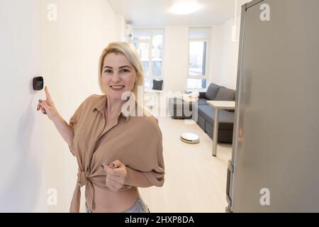 Gros plan de la femme réglant la température du chauffage central à la maison sur le thermostat. Banque D'Images