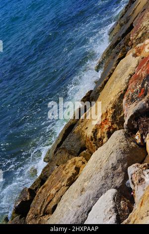 De petites vagues frappent des rochers humides en bord de mer par une journée ensoleillée Banque D'Images