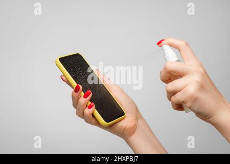 Les mains des femmes vaporisent du désinfectant sur le téléphone portable pour nettoyer et protéger contre les virus. Nettoyage du smartphone avec un désinfectant pour les mains à base d'alcool. Banque D'Images
