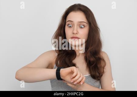 Une jeune fille aux cheveux longs regarde sa montre de poignet en surprise Banque D'Images