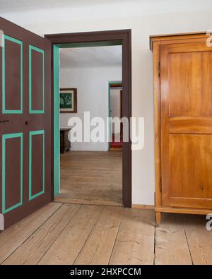 ancienne porte peinte en brun-vert avec vue sur la deuxième chambre, coffre en bois à droite et parquet Banque D'Images