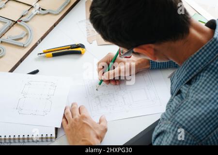 Concepteur de boîtes qui travaille dur et qui fait un croquis sur papier avec un crayon, chassés dessus. Assis derrière le bureau, dessin. De l'arrière. Banque D'Images