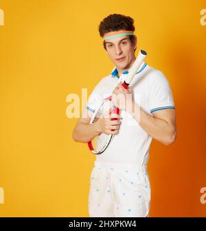 Comment le retenir à nouveau ? Un jeune homme dans une tenue de tennis rétro tenant sa raquette comme un quitar. Banque D'Images