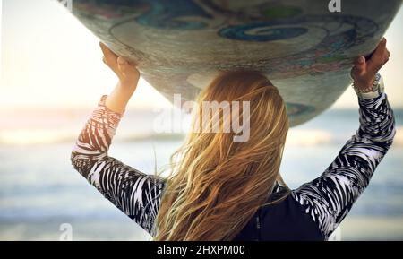 En direction de l'océan. Vue arrière d'une jeune surfeuse méconnue debout avec sa planche de surf qui donne sur l'océan. Banque D'Images
