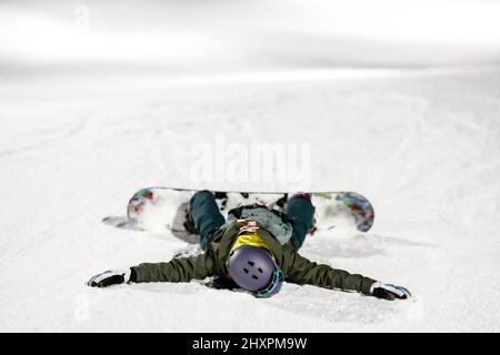 Fille de snowboardeur couchée face vers le bas sur la pente. Ski de nuit dans la station d'hiver. Banque D'Images