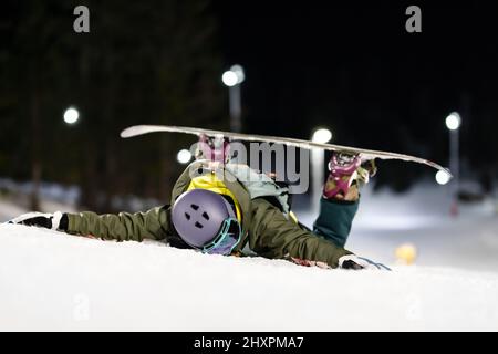 Fille de snowboardeur couchée face vers le bas sur la pente. Ski de nuit dans la station d'hiver. Banque D'Images