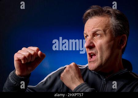 Homme blanc d'âge moyen en position de boxe sur fond noir et bleu Banque D'Images