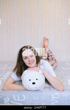 Jeune femme souriante heureuse, mariée au lit en pyjama, peignoir dans une maison confortable. Eau potable. Détendez-vous. Un mode de vie sain. Rituels du matin. Banque D'Images