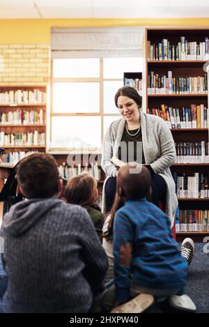 Shes partage son amour pour les livres à la classe. Photo d'un enseignant lisant à un groupe d'enfants du primaire dans la bibliothèque. Banque D'Images