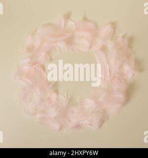 Couronne de plumes pastel roses sur fond jaune minimal avec espace de copie circulaire. Banque D'Images