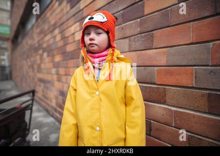 Petite fille avec le syndrome de Down regardant les caméras outoors en hiver contre le mur de brique. Banque D'Images