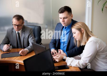 Les professionnels assis au bureau parlent et utilisent des ordinateurs portables et des tablettes Banque D'Images