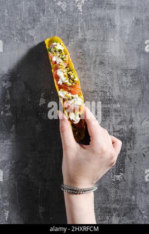 tacos au maïs avec saumon, mayonnaise et pistaches sur une table en béton et une main femelle Banque D'Images