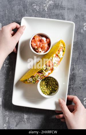 tacos au maïs avec saumon, mayonnaise et pistaches sur une table en béton et une main femelle Banque D'Images