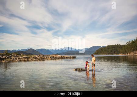 Un homme se tient dans l'eau peu profonde avec deux jeunes enfants dans la grande baie Banque D'Images