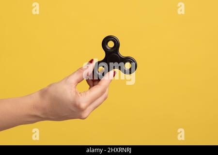 Gros plan vue latérale profil portrait de femme main tenant le spinner noir de violon, jouet soulageant le stress. Studio d'intérieur isolé sur fond jaune. Banque D'Images