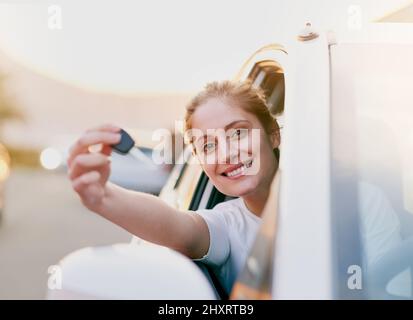Allons sur la route. Portrait d'une jeune femme tenant les clés de sa voiture tout en étant assise à l'intérieur. Banque D'Images
