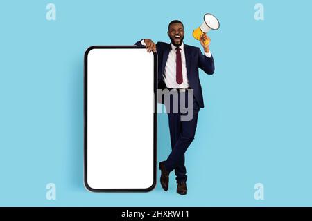 Offre exceptionnelle. Homme d'affaires noir enthousiaste utilisant Megaphone tout en se tenant près de smartphone Blank Banque D'Images