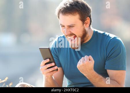 Un homme enthousiaste qui trouve de bonnes nouvelles sur un smartphone et qui célèbre l'extérieur Banque D'Images