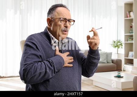 Homme mature qui fume et tousse à la maison dans une salle à manger Banque D'Images