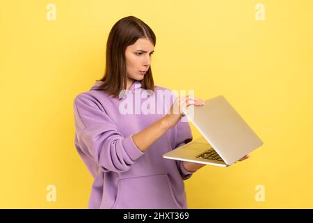 Portrait d'une femme curieuse concentrée regardant dans un cahier à moitié ouvert, espionnant, veut voir les informations interdites, portant le pull à capuche violet. Studio d'intérieur isolé sur fond jaune. Banque D'Images
