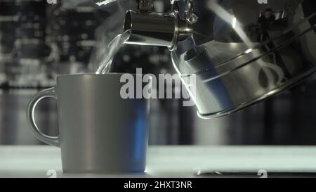 Gros plan sur le versement d'eau bouillie chaude de la bouilloire à gaz en acier poli dans la tasse. Action. Ambiance chaleureuse dans la cuisine dans les couleurs grises à la maison. Banque D'Images