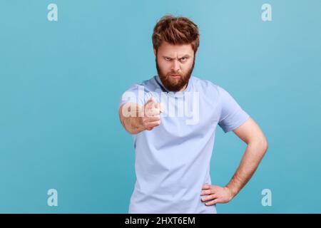 Hé vous. Portrait d'un jeune adulte mécontent homme barbu et bosseux pointant le doigt vers l'appareil photo et accusant les erreurs, vous rendant coupable. Studio d'intérieur isolé sur fond bleu. Banque D'Images