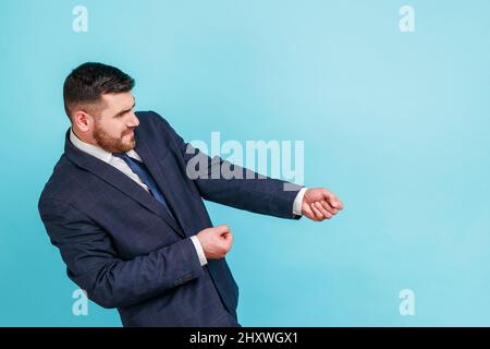 Portrait d'un homme d'affaires ambitieux et fort en costume prétendant tirer la corde invisible, concept de travail dur, effort et efforts pour atteindre des réalisations. Studio d'intérieur isolé sur fond bleu. Banque D'Images