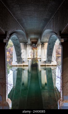 Tiré de sous un vieux pont avec des arches avec des reflets visibles sur l'eau calme de la forêt Banque D'Images