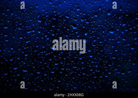 La pluie d'eau tombe sur une surface bleu profond comme arrière-plan. Toile de fond abstraite. Banque D'Images