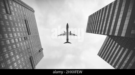 Vue en bas angle d'un avion volant au-dessus des gratte-ciel, prise en niveaux de gris Banque D'Images