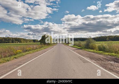 Paysage avec route d'automobile asphaltée à travers le champ vert et nuages sur le ciel bleu en été. Banque D'Images
