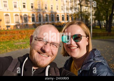 Couple heureux dans le sourire d'amour et de faire selfie en ville. Style de vie des personnes magnifiques. Homme bald en lunettes et femme attrayante en lunettes de soleil. Banque D'Images