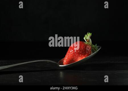 Gros plan d'une fraise sur une cuillère d'argent et un fond noir Banque D'Images