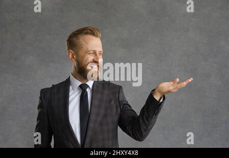 Un bel homme barbu dans une chemise blanche et une veste noire avec un sourire démontre un produit imaginaire Banque D'Images