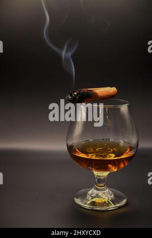 Prise verticale d'un cigare allumé sur un verre de whisky Banque D'Images