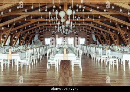 Vue sur une salle de réception ou de mariage avec de longues tables et chaises blanches et plafond à poutres apparentes Banque D'Images