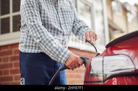 Gros plan de l'homme qui attache le câble de chargement à la voiture électrique écologique sans émission à la maison Banque D'Images