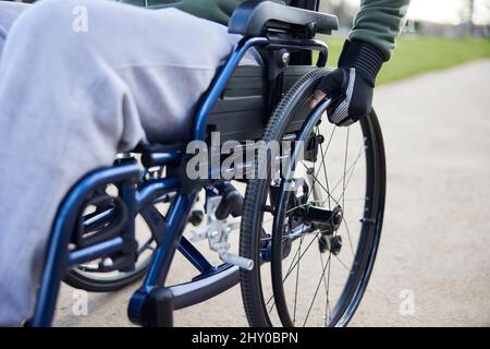 Gros plan d'un adolescent portant des gants de protection en fauteuil roulant dans le parc Banque D'Images