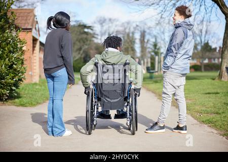 Adolescent en fauteuil roulant, qui se laque et rit avec ses amis à Park Banque D'Images