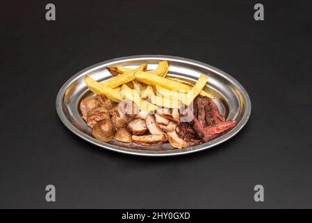 Asado de viandes et chorizos assortis avec des frites maison sur une plaque en acier inoxydable Banque D'Images